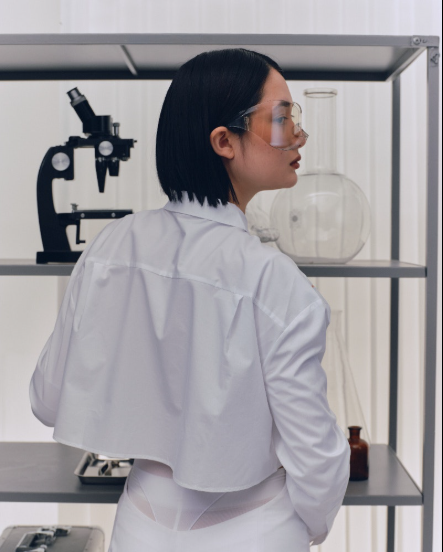 Woman in lab coat and safety glasses in laboratory with microscope and glassware, skincare research