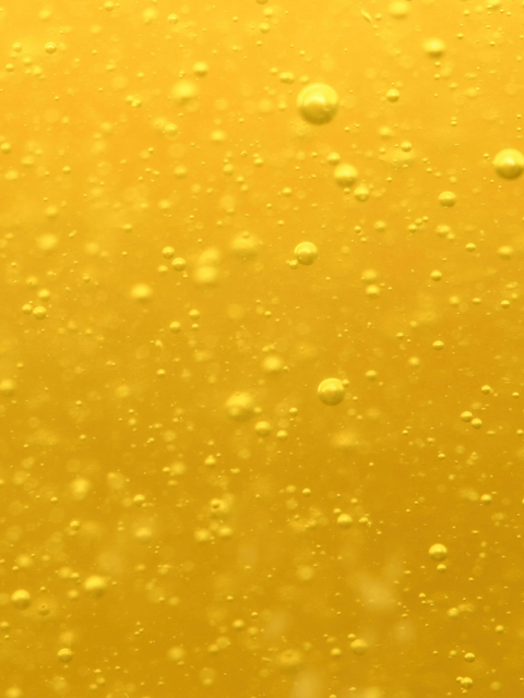 Yellow facial oil serum with bubbles, suitable for hydration, main ingredient botanical oil, shown in dropper bottle close-up.